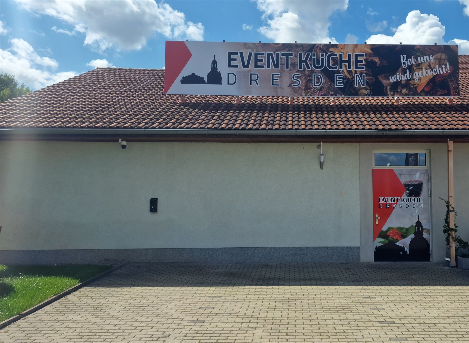 Eingang der Event-Küche Dresden bei Tageslicht mit blauem Himmel, darüber das Banner auf dem Dach