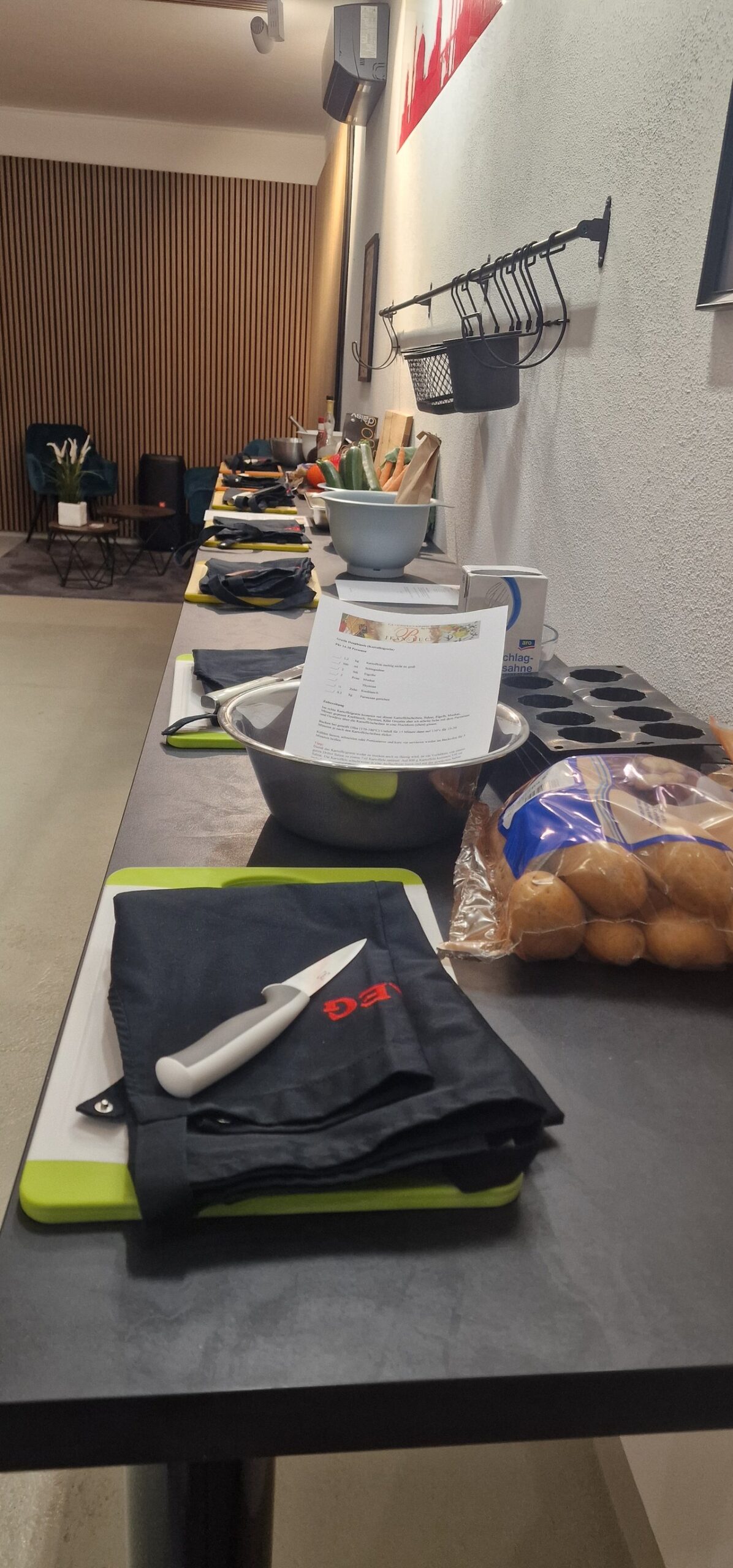 Vorbereitete Arbeitsplätze entlang der Kochinsel: Schneidbretter, Schürzen, Messer und Zutaten