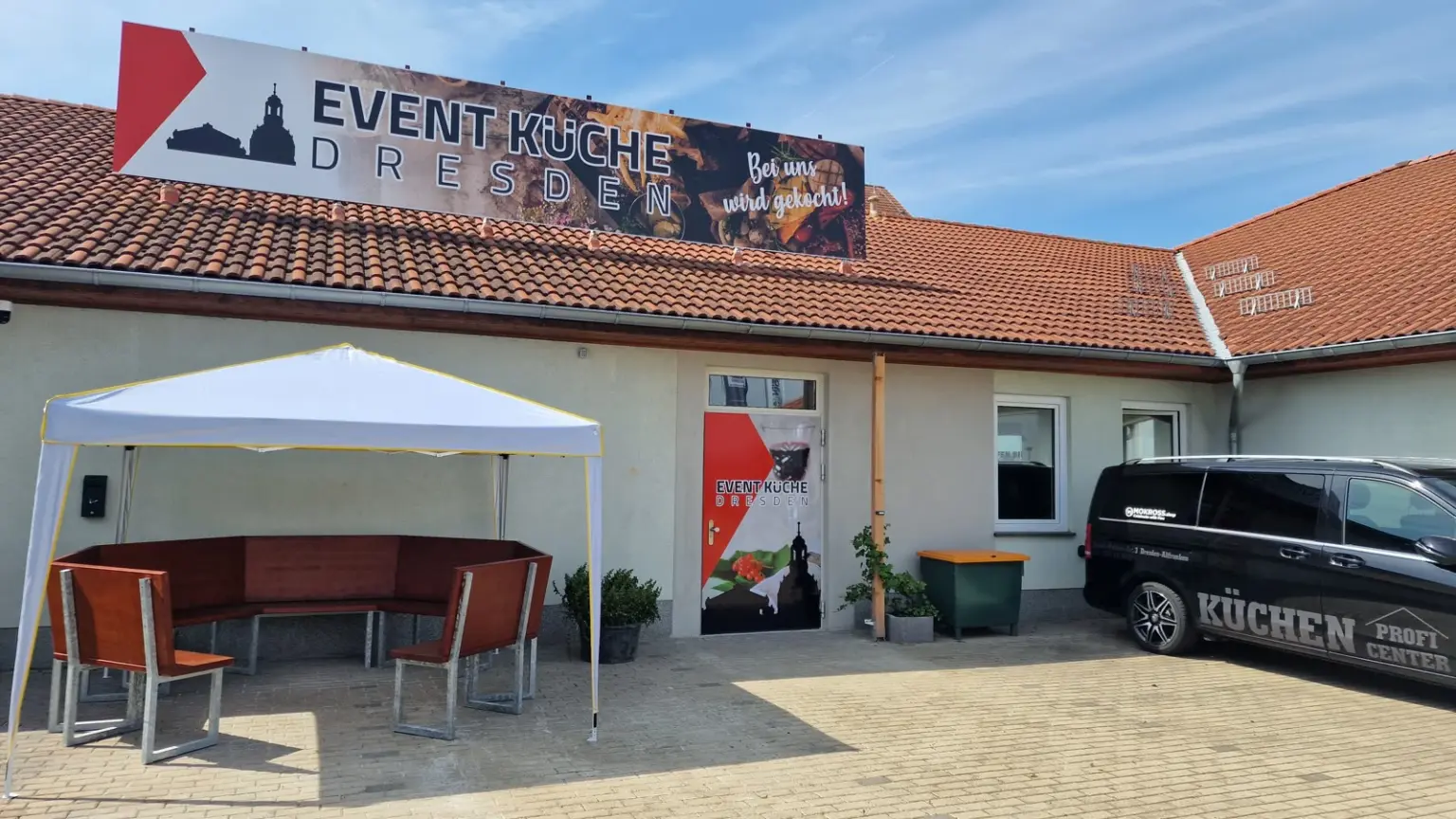 Pavillon mit Sitzgruppe auf dem Hof der Event-Küche Dresden, dahinter das Gebäude mit Banner